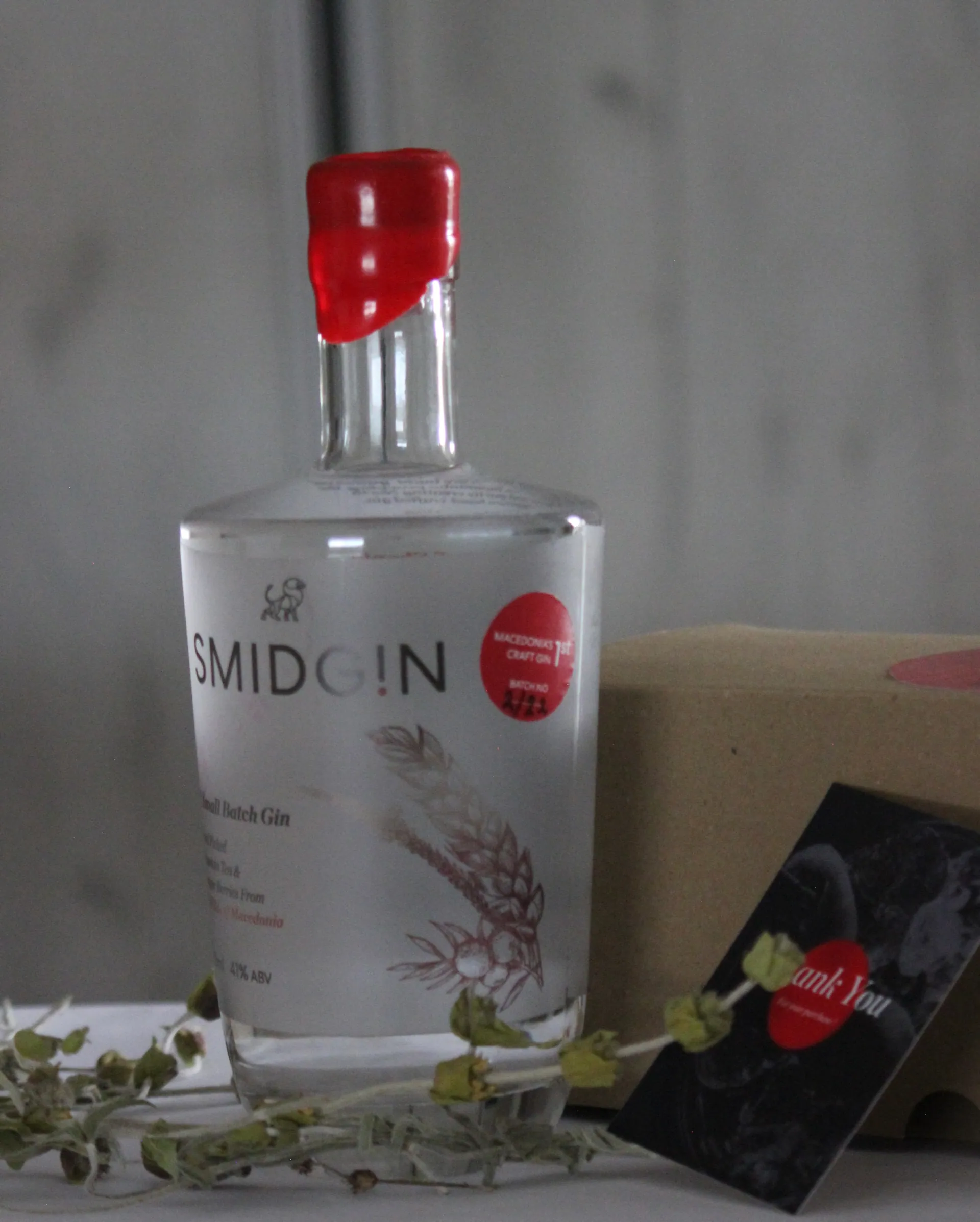 An empty Smidgin bottle with its red wax seal, beside dried botanicals and a gift box